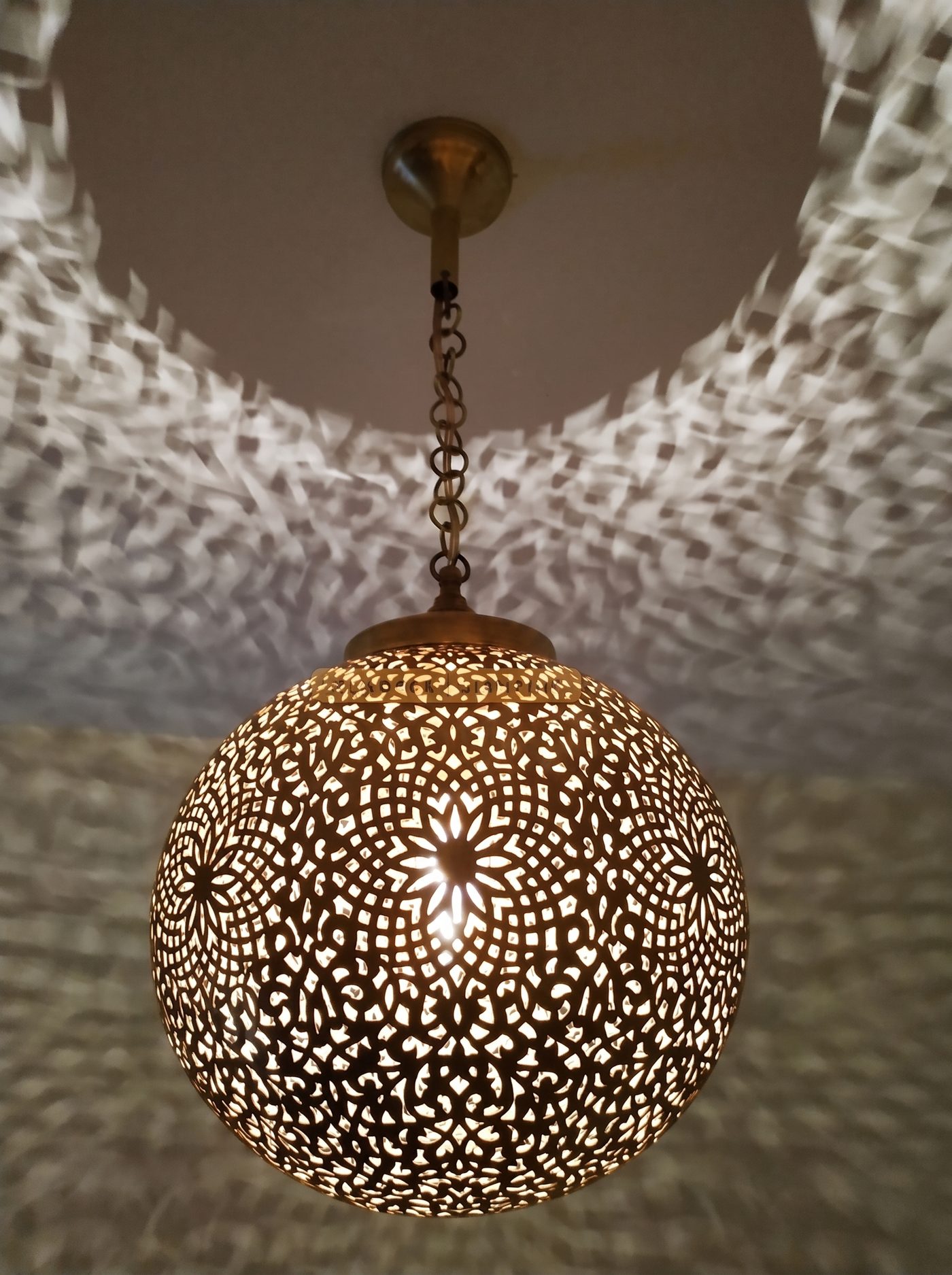 A lit brass sphere pendant throwing star patterns across the walls